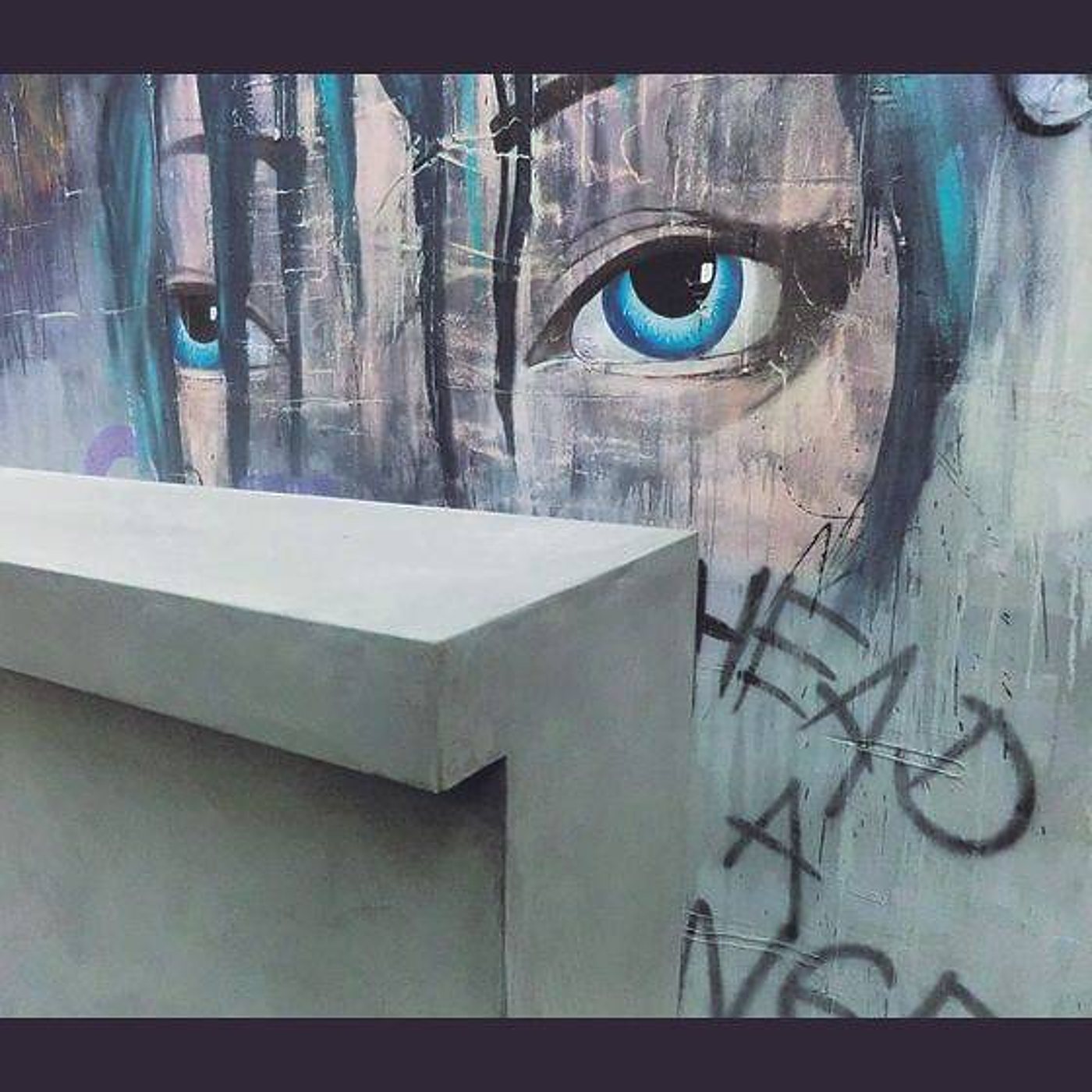 Un comptoir en béton gris se tient devant un mur orné d’une grande fresque représentant un visage aux yeux bleus et aux cheveux turquoise.